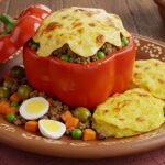 Pimentão vermelho recheado com carne moída, legumes, ovo e coberto com queijo gratinado, acompanhado de batatas ao forno em prato rústico peruano