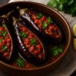 Berinjelas recheadas com tomates e cebolas caramelizadas, servidas em caçarola rústica turca, acompanhadas de limão e salsa fresca.