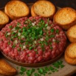 Carne de onça servida em prato rústico de cerâmica, carne bovina crua moída temperada com cebola, cheiro-verde e azeite, acompanhada de torradas douradas sobre mesa de madeira.